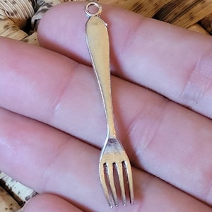 Op de afbeelding: Zilverkleurige vorkcharm met een lus aan de bovenkant om aan een ketting of armband te bevestigen. De vork is ongeveer 5 cm lang.
