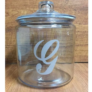 May include: Clear glass jar with a lid and a white letter G etched on the front.