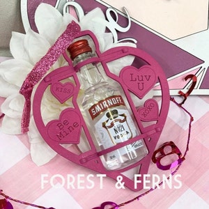 May include: Pink heart-shaped wooden frame with a miniature bottle of Smirnoff No. 21 vodka inside. The frame has the words "Be Mine", "Kiss", "Luv U", and "xoxo" written on it.