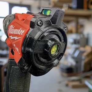 May include: A red and black Milwaukee Fuel power drill featuring a custom-fitted black 3D-printed attachment on the back. This accessory includes two integrated circular spirit levels, one positioned on the top and one centered on the rear housing.