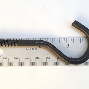 May include: A black metal screw hook with a 3-inch length. The hook is measured against a ruler.