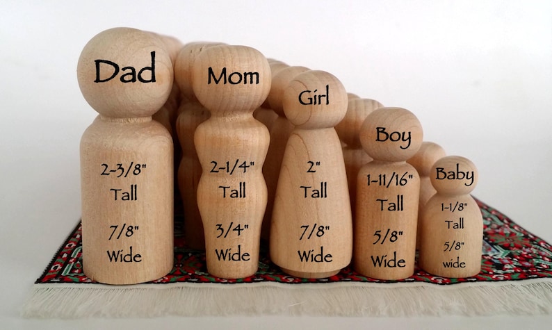 May include: A collection of unfinished light-colored wooden peg dolls in various sizes. Each figure is labeled with its role and dimensions in inches: Dad 2-3/8" tall, Mom 2-1/4" tall, Girl 2" tall, Boy 1-11/16" tall, and Baby 1-1/8" tall.