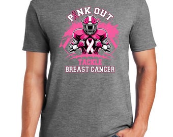Puede incluir: Camiseta gris con un diseño rosa y blanco. El diseño presenta un jugador de fútbol americano con casco y uniforme rosa, con el texto "PINK OUT" y "TACKLE BREAST CANCER". También incluye una cinta rosa.