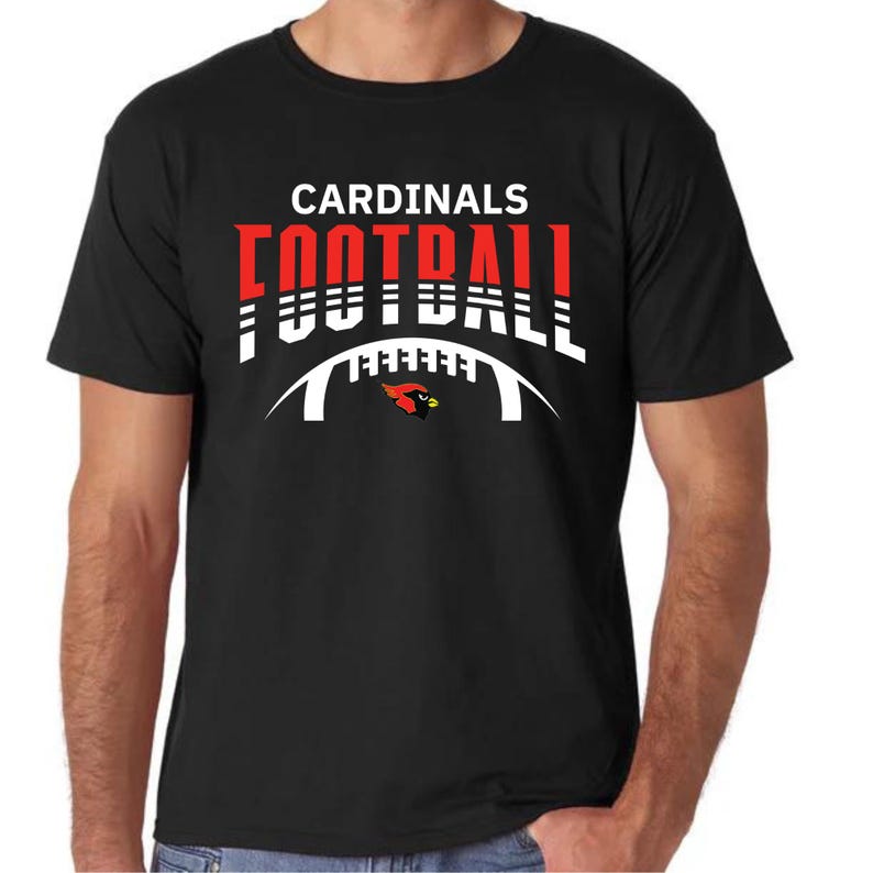 Peut inclure: T-shirt noir avec un motif graphique blanc et rouge qui dit "CARDINALS FOOTBALL" avec un oiseau cardinal rouge et une arche de football blanche.