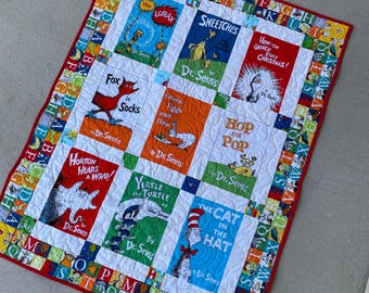 Könnte beinhalten: Eine rechteckige Steppdecke mit einem Patchwork-Design aus neun Dr. Seuss-Buchcovern, darunter The Lorax, Sneetches, How the Grinch Stole Christmas, Fox in Socks, Green Eggs and Ham, Hop on Pop, Horton Hears a Who, Yertle the Turtle und The Cat in the Hat.