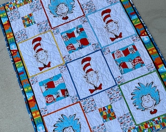 Könnte beinhalten: Eine Patchwork-Decke mit den Charakteren aus Dr. Seuss' Der Kater mit Hut, darunter der Kater mit seinem rot-weiß gestreiften Hut sowie Ding Eins und Ding Zwei mit blauem Haar. Der bunte Rand ist mit dem Text The Cat in the Hat versehen.