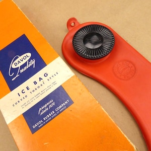 May include: An orange and blue Davol Ice Bag box and a red curved throat style ice bag. The box has the text "Davol Quality" and "Ice Bag Curved Throat Style". The red ice bag has a black circular cap.