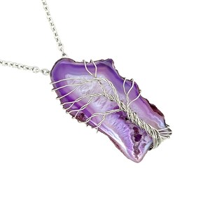 Könnte beinhalten: Ein Anhänger aus violettem Achat mit einem Baumdesign aus Silberdraht. Der Anhänger ist an einer silbernen Kette.