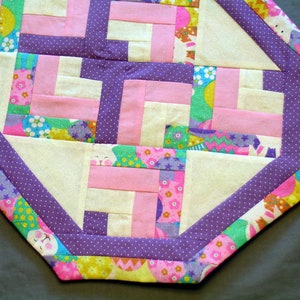 May include: A purple and pink patchwork table runner with a white background and a white polka dot border. The runner features a variety of Easter-themed fabrics with bunnies, eggs, and flowers.
