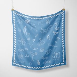 May include: A square blue scarf with a white checkered border featuring white line-art illustrations of a sailboat, ship wheel, rings, a cocktail, cherries, and text including Charleston, Folly Beach, King St, BZ+CSF, and the date 11.08.25.
