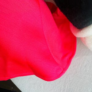 Może przedstawiać: Zbliżenie na jasnor&oacute;żową tkaninę o fakturowanej powierzchni. Tkanina ma zakrzywiony brzeg i jest zszyta r&oacute;żową nicią.