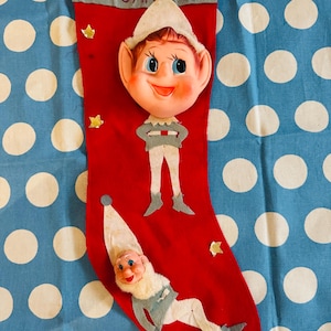 Può includere: Una calza di Natale rossa vintage con un'applicazione di viso e corpo di elfo. La calza ha il nome "SUSAN" ricamato sulla parte superiore. Accenti di stelle dorate sono sparsi sulla calza.