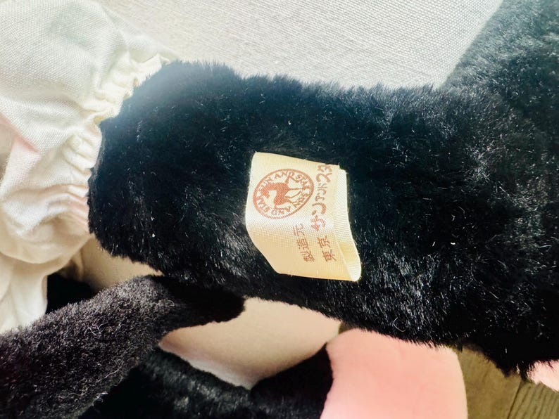 Może przedstawiać: Pluszowa zabawka w kolorze czarno-białym z brązową metką, na kt&oacute;rej widnieje napis "Pony and Bear" w języku japońskim. Metka zawiera r&oacute;wnież obrazek konia i niedźwiedzia.