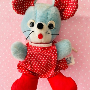 May include: A blue plush mouse wearing a red dress with white polka dots. The mouse has large black eyes and a red nose. The tag on the mouse reads "ALS Dolls Mark Material."
