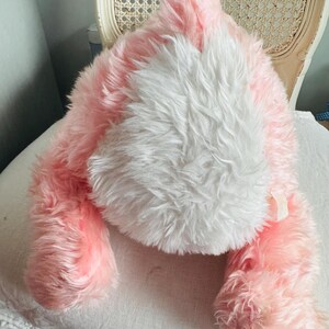 May include: A plush pink and white bunny rabbit toy. The bunny has long, fluffy fur in shades of pink and white. The toy is lying down, with its ears and paws visible. The toy is soft and cuddly, perfect for children.