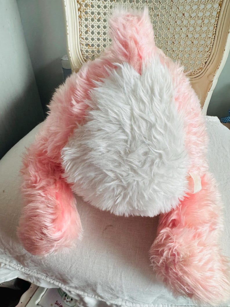 May include: A plush pink and white bunny rabbit toy. The bunny has long, fluffy fur in shades of pink and white. The toy is lying down, with its ears and paws visible. The toy is soft and cuddly, perfect for children.