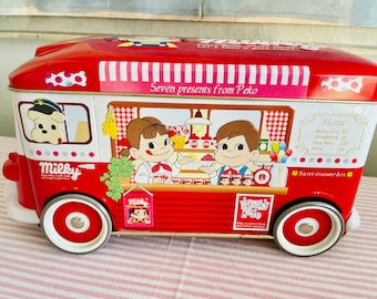 May include: Red and white tin box shaped like a delivery truck with a cartoon character on the side. The box says "Seven presents from Peko" and "Milky".