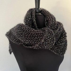 May include: A dark gray and white knit infinity scarf displayed on a black mannequin. The scarf is made of a chunky knit with a mix of dark gray and white threads, creating a textured appearance. The scarf is draped to show its circular shape.