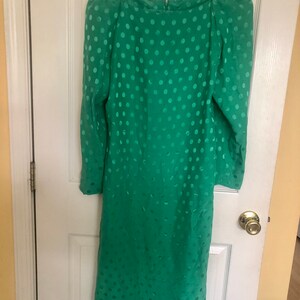 Op de afbeelding: Een groene polkadotjurk met een ronde hals en lange mouwen. De jurk heeft strassversieringen op de schouders.