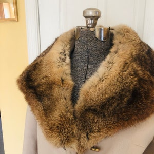 May include: A vintage beige coat with a luxurious brown fur collar. The coat is displayed on a mannequin, showcasing the collar's rich texture and color variations. A gold button adds a touch of elegance to the coat's design.