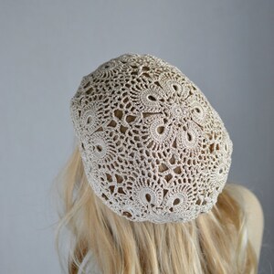 May include: A beige crocheted beret with a delicate, lacy pattern.