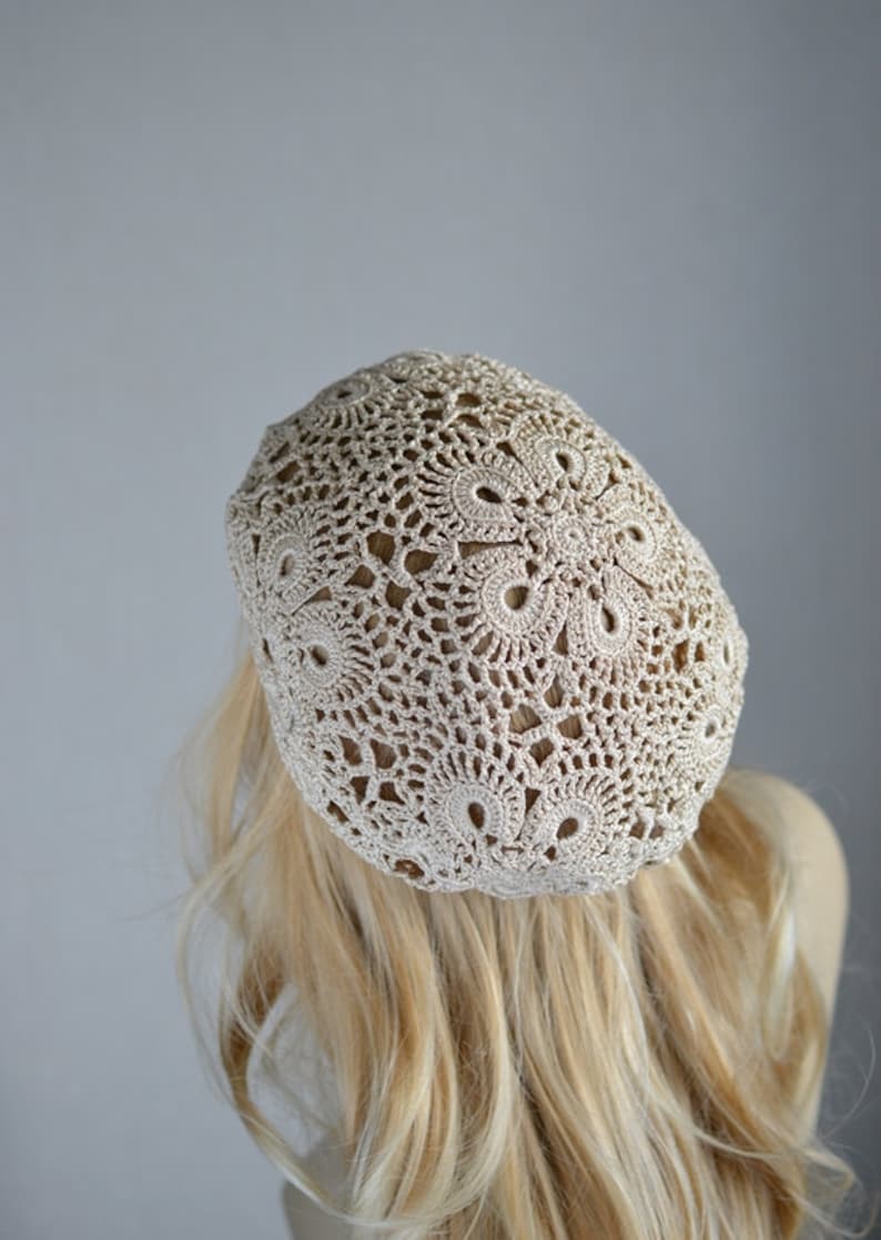 May include: A beige crocheted beret with a delicate, lacy pattern.