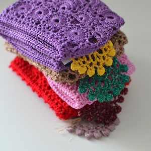 May include: A stack of six crocheted doilies in various colours, including purple, brown, red, pink, green, and burgundy. The doilies are layered on top of each other, with the purple doily on top.
