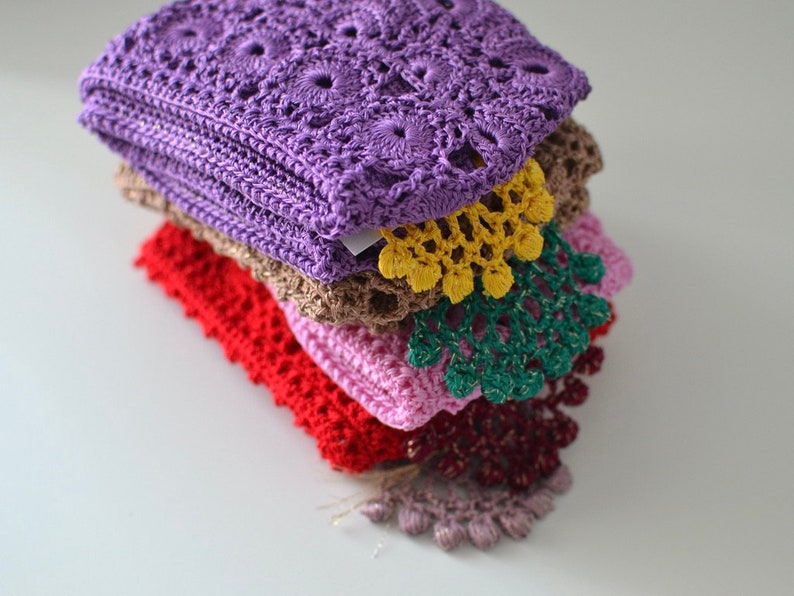 May include: A stack of six crocheted doilies in various colours, including purple, brown, red, pink, green, and burgundy. The doilies are layered on top of each other, with the purple doily on top.