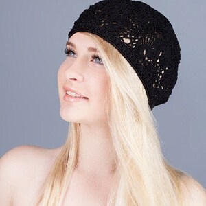 May include: A woman with long blonde hair is wearing a black crocheted beret. The beret has a delicate openwork design.