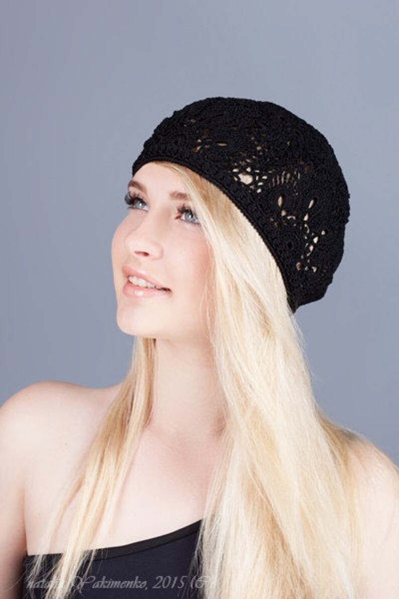 May include: A woman with long blonde hair is wearing a black crocheted beret. The beret has a delicate openwork design.