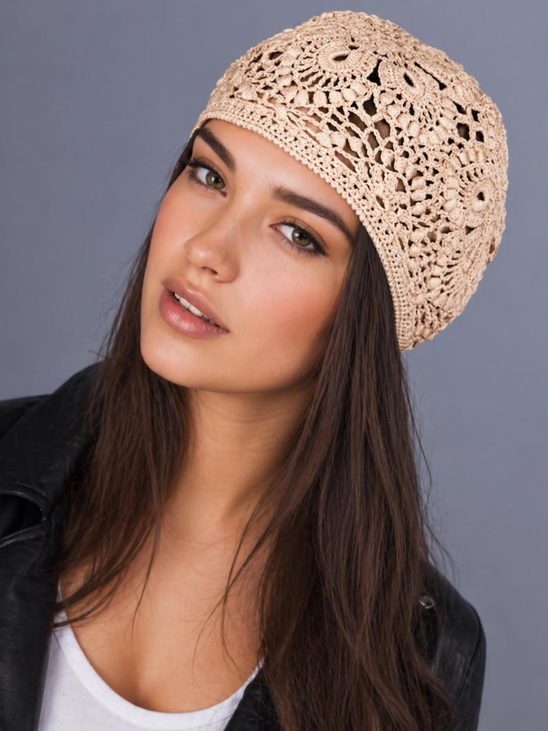 May include: A beige crocheted hat with an openwork design. The hat is made of a light-colored yarn and has a rounded shape. The hat is worn on the head. The background is a solid gray color.