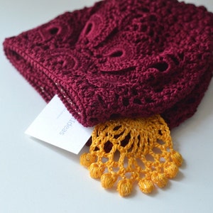 May include: A burgundy crocheted hat with a yellow crocheted trim. The hat is folded in half and the trim is visible on the bottom.