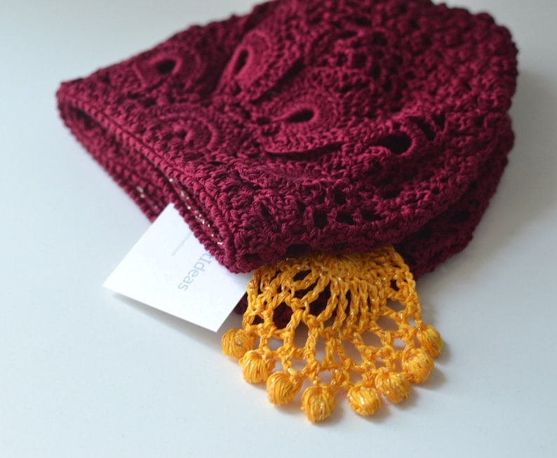 May include: A burgundy crocheted hat with a yellow crocheted trim. The hat is folded in half and the trim is visible on the bottom.