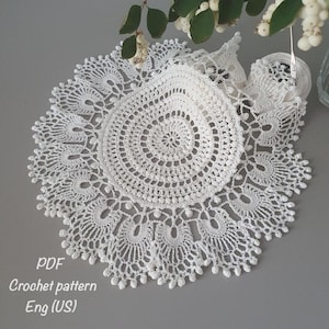 May include: White crochet doily with a delicate, intricate design. The doily is circular and has a scalloped edge. The pattern includes a central circle with concentric rings of smaller circles. The doily is made with fine thread and has a delicate, airy feel. PDF Crochet pattern Eng (US)