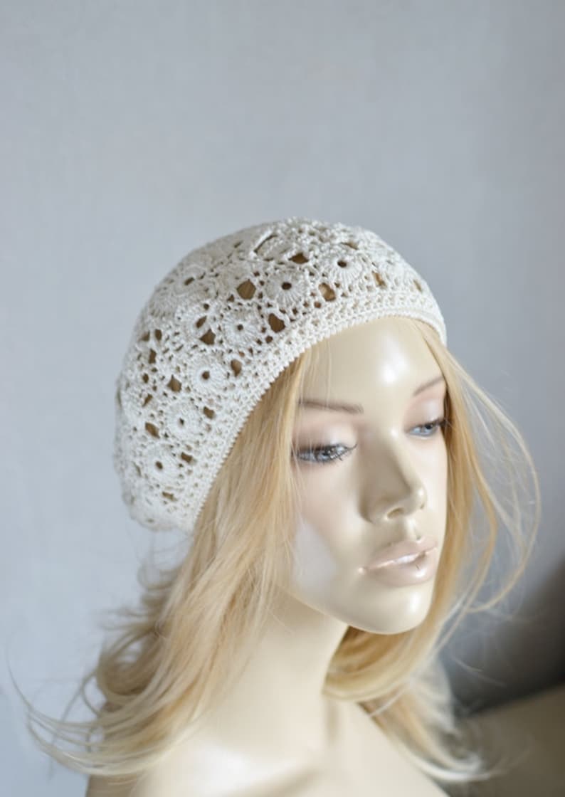 May include: A white crocheted beret with a delicate openwork pattern. The beret is worn on a mannequin with blonde hair.