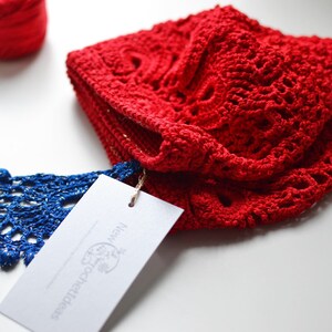 May include: Red crocheted hat with a blue and gold crocheted tassel. The hat is folded and has a white tag with the text "New Together" on it.