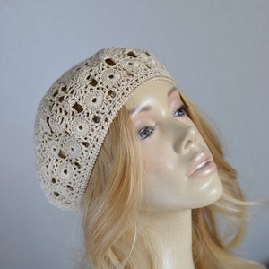 May include: A beige crocheted beret with a delicate floral pattern.