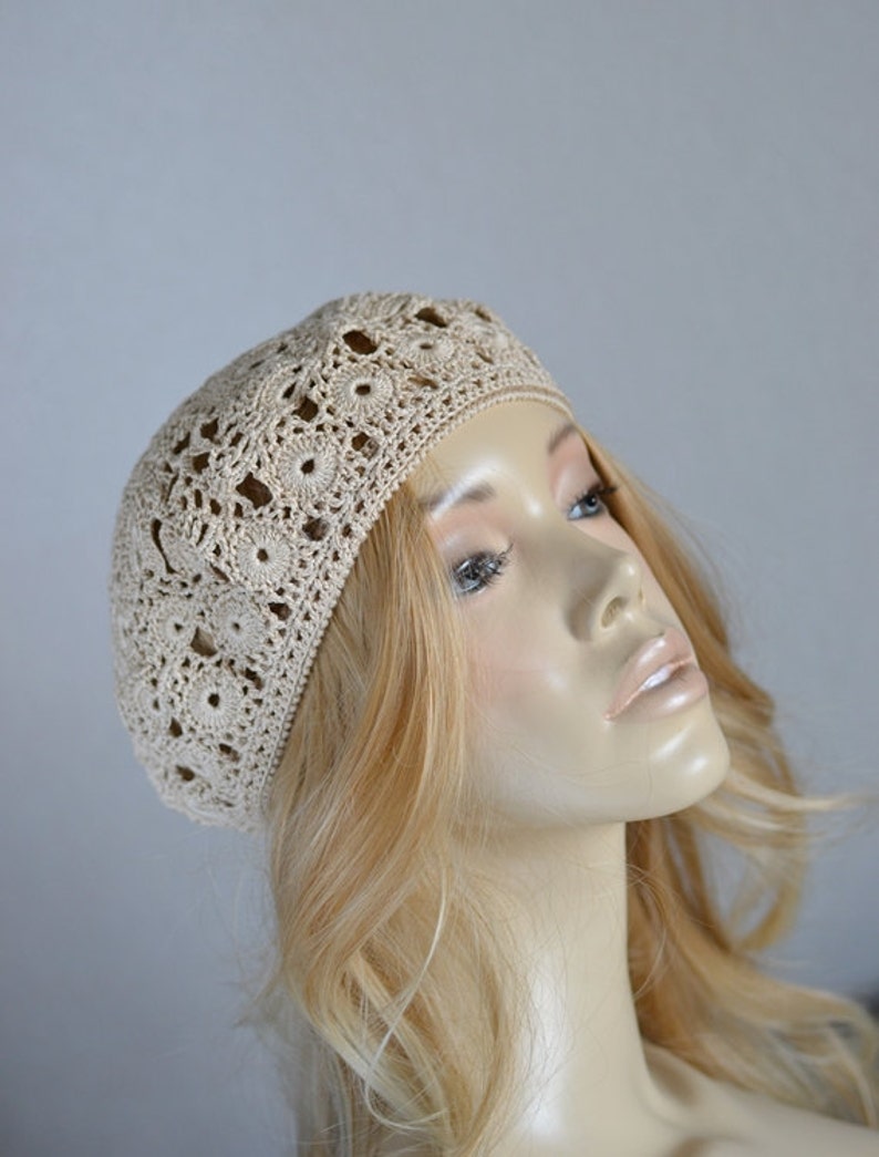 May include: A beige crocheted beret with a delicate floral pattern.