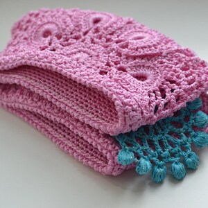 May include: A pink crocheted blanket with a blue crocheted trim. The blanket is folded in half and the trim is visible on the bottom edge.
