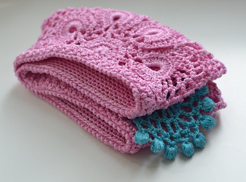 May include: A pink crocheted blanket with a blue crocheted trim. The blanket is folded in half and the trim is visible on the bottom edge.
