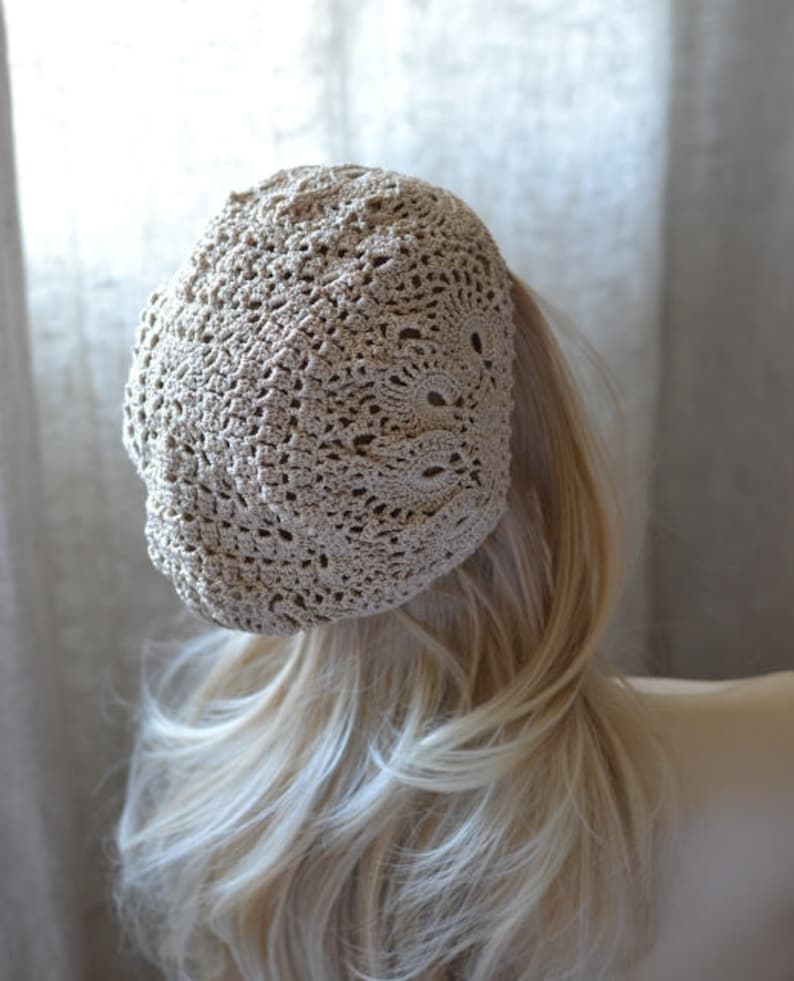 May include: A beige crocheted beret with a delicate openwork pattern. The beret is worn on a mannequin with long blonde hair.