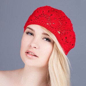May include: A woman with blonde hair is wearing a red crocheted beret. The beret has a delicate floral pattern.