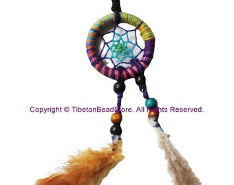 May include: A vibrant dreamcatcher featuring a woven web and feathers. The circular frame is wrapped in rainbow-coloured yarn, with a blue and green web at the centre. Black and wooden beads hang below, along with brown and white feathers.