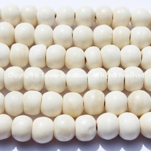May include: Rows of off-white, rounded beads with a slightly flattened shape. The beads are strung together, creating a textured surface. The beads are uniform in size and color, with a matte finish. The image is well-lit, highlighting the details of the beads.
