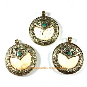 Peut inclure: Trois pendentifs ronds avec des ornements en métal argenté. Chaque pendentif présente une incrustation crème en forme de cœur et une petite pierre turquoise. Les pendentifs ont une boucle dorée en haut pour les suspendre.