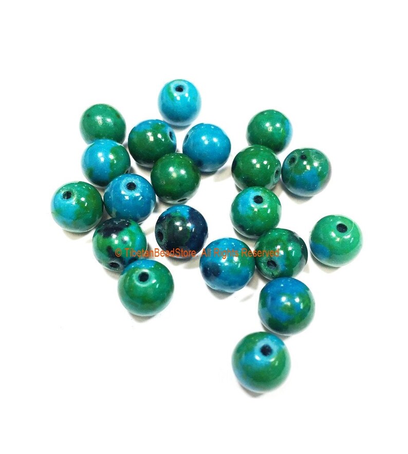 May include: A collection of 20 round, green and blue beads. The beads are made of a smooth, polished material and have a mottled appearance.
