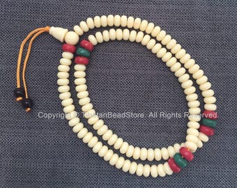May include: Cream-colored prayer beads with red and green accent beads. The beads are strung together in two strands, with a tassel and two black beads at the end. The text "Copyright © TibetanBeadStore. All Rights Reserved." is visible.