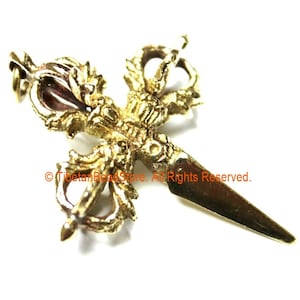 May include: A gold-colored metal pendant in the shape of a Tibetan ritual dagger, known as a Phurba. The dagger has a double-headed design with intricate details and a sharp point.