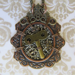Puede incluir: Un colgante de estilo steampunk de cobre y latón con un diseño en forma de llave, engranajes y otros detalles intrincados.