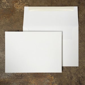 May include: Two white envelopes, one slightly larger than the other, are lying flat on a brown textured surface. The larger envelope has a strip of white tape across the top.